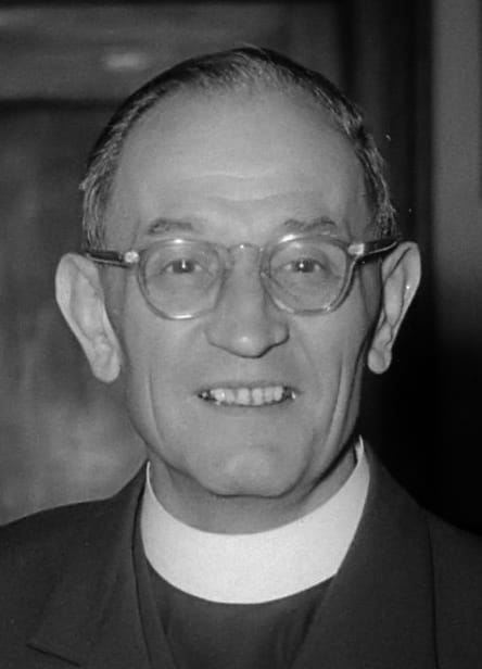 A black-and-white photo portrait of a white man wearing spectacles and a clerical collar.