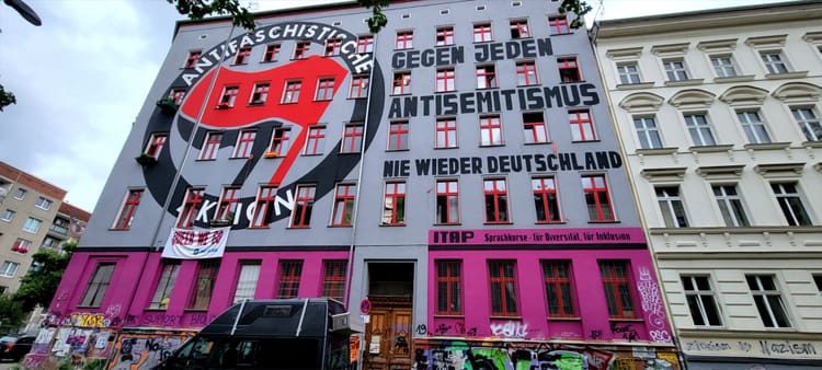 A painted mural on the exterior of an apartment building reads: 'Antifaschistische Aktion - Gegen Jeden Antisemitismus nie wieder Deutschland.'
