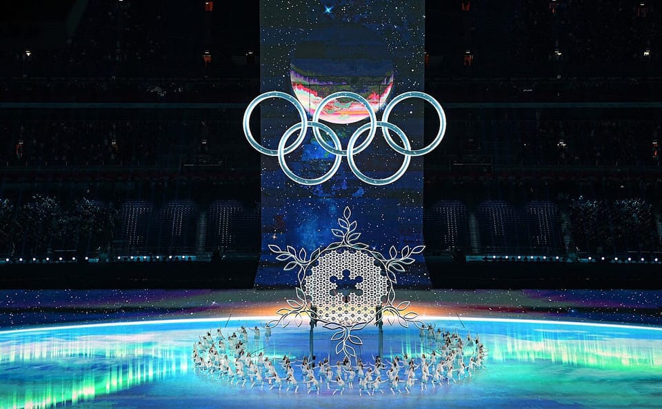 A blue-hued skating rink is topped by a dark ceiling that resembles the night sky. An image of the planet Earth hangs above the ice, with the Olympic Rings just below it.